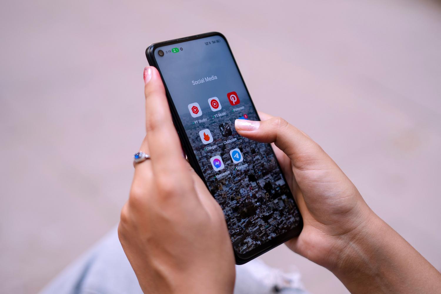 Manos sosteniendo un teléfono móvil con diversas aplicaciones de redes sociales abiertas, representando el uso de herramientas digitales para mejorar el perfil.