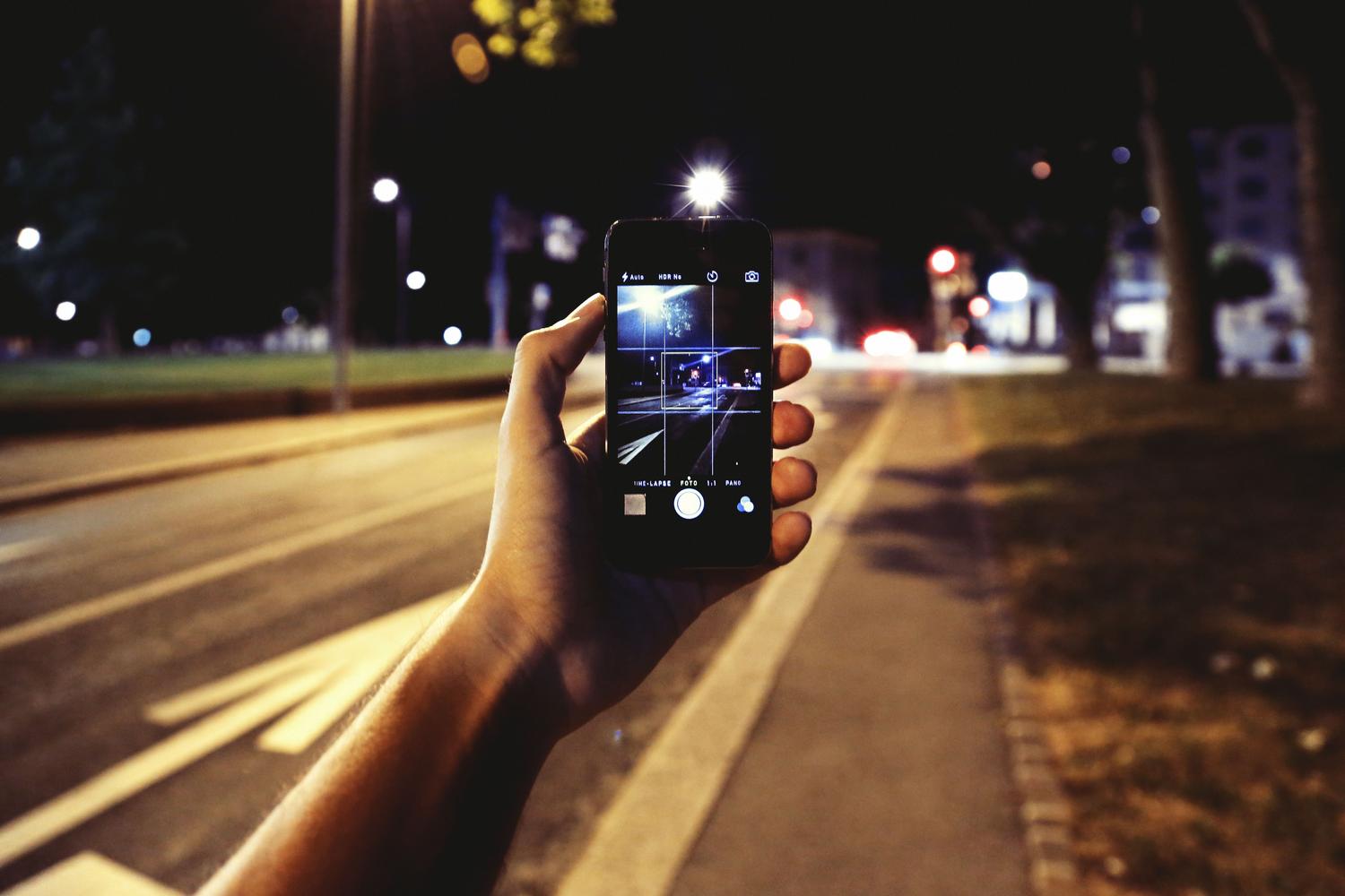 Primer plano de una mano usando un móvil para fotografiar una calle vibrante e iluminada de noche