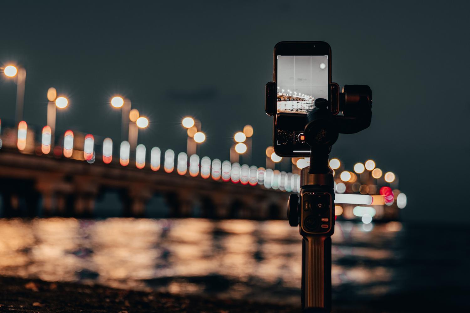 Smartphone montado en un trípode capturando una escena nocturna de un muelle con luces al fondo