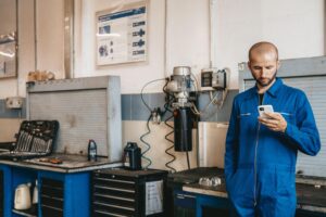 Técnico mecánico utilizando un smartphone en su taller para gestionar órdenes de servicio