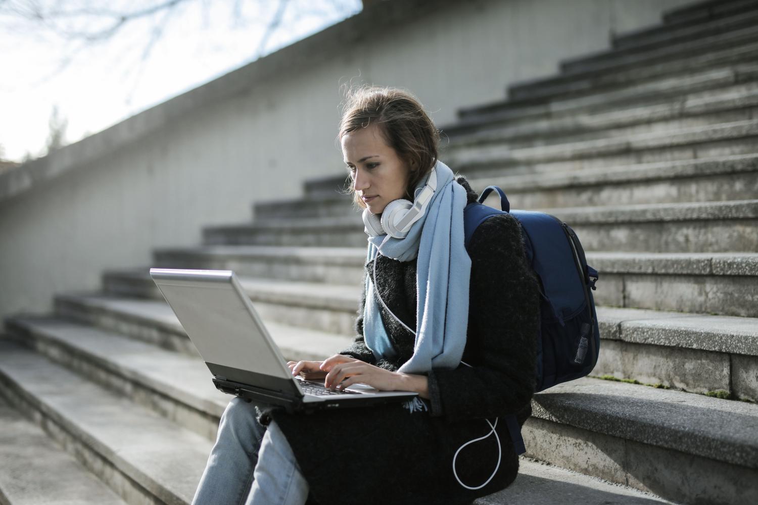 Estudiante utilizando un portátil y auriculares al aire libre, representando el aprendizaje flexible y personalizado.