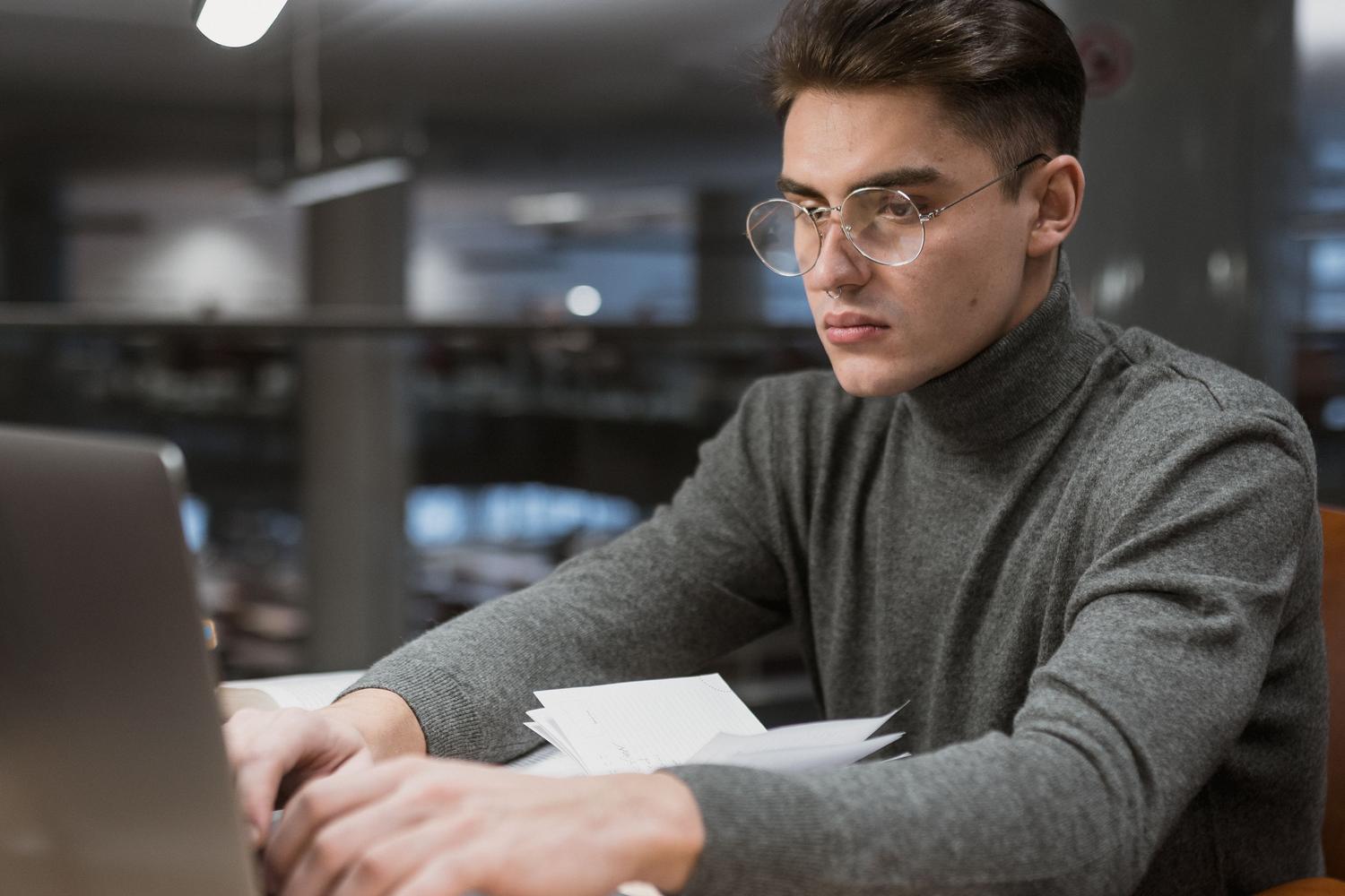 Estudiante en la biblioteca realizando una investigación profunda combinando notas físicas y digitales.
