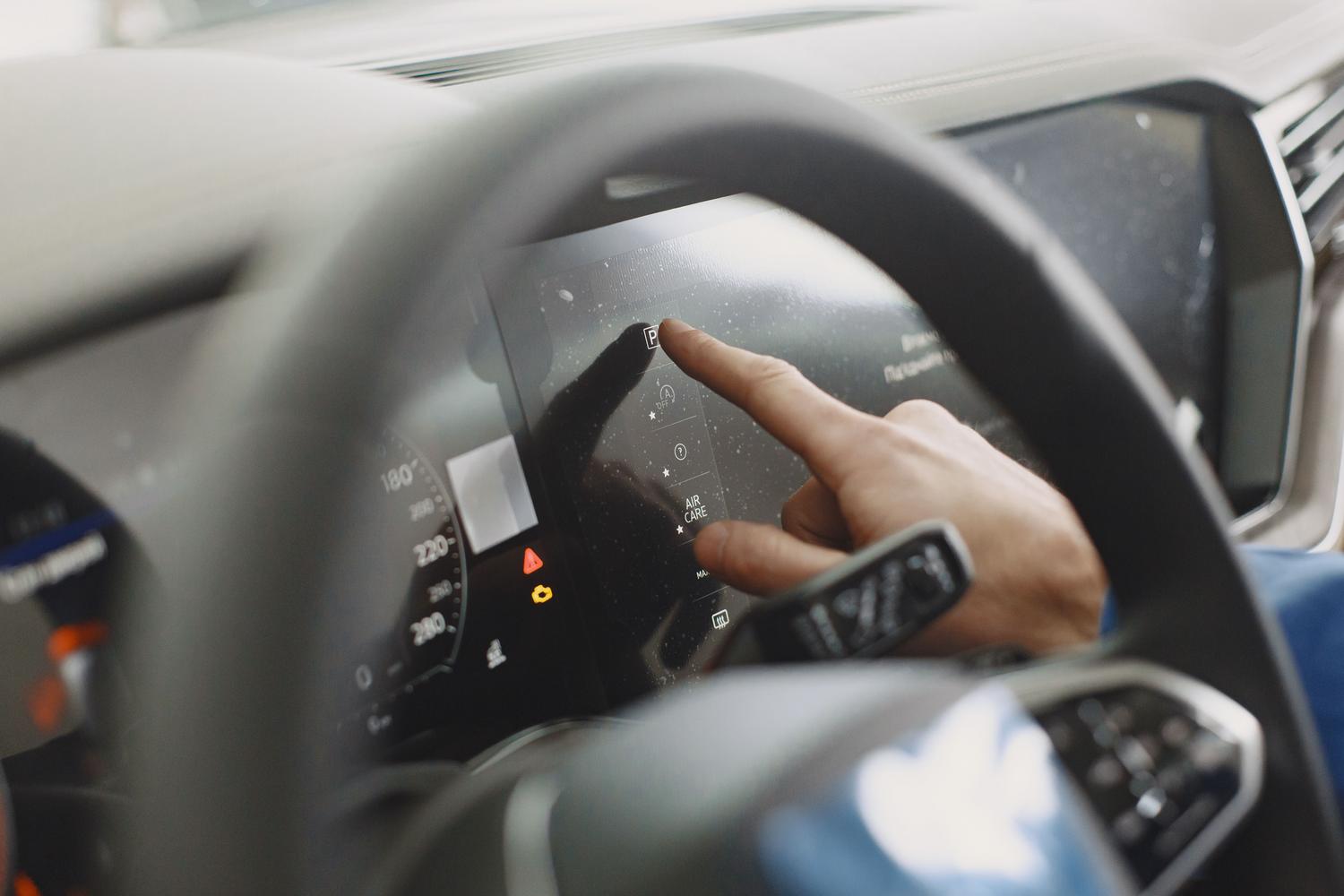Mano interactuando con el panel digital de un coche moderno, configurando los sistemas de asistencia al conductor.