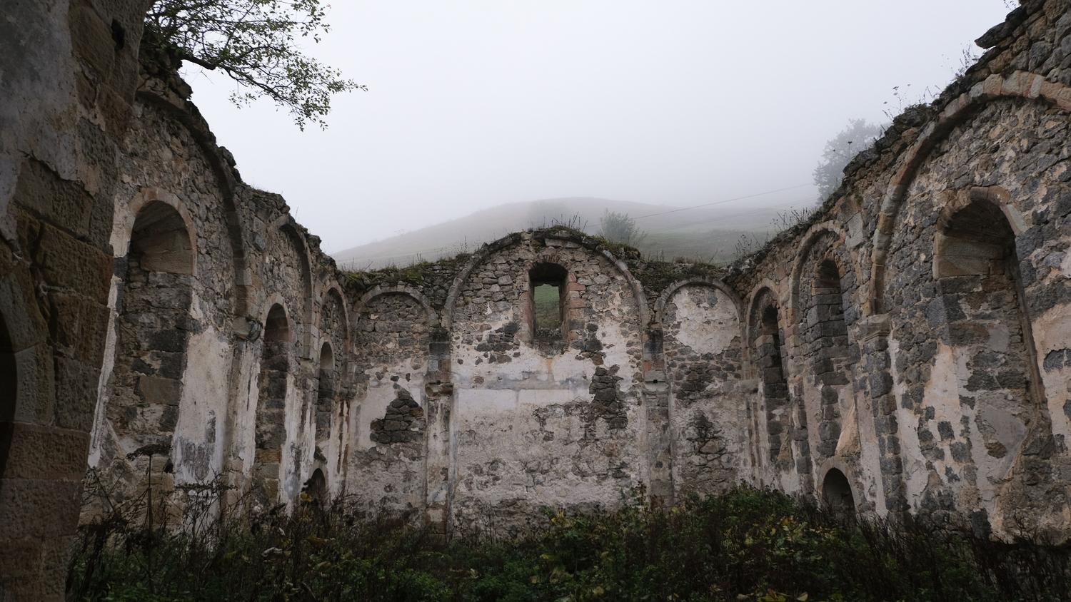 Ruinas de piedra de un antiguo monasterio envueltas en una densa niebla gris