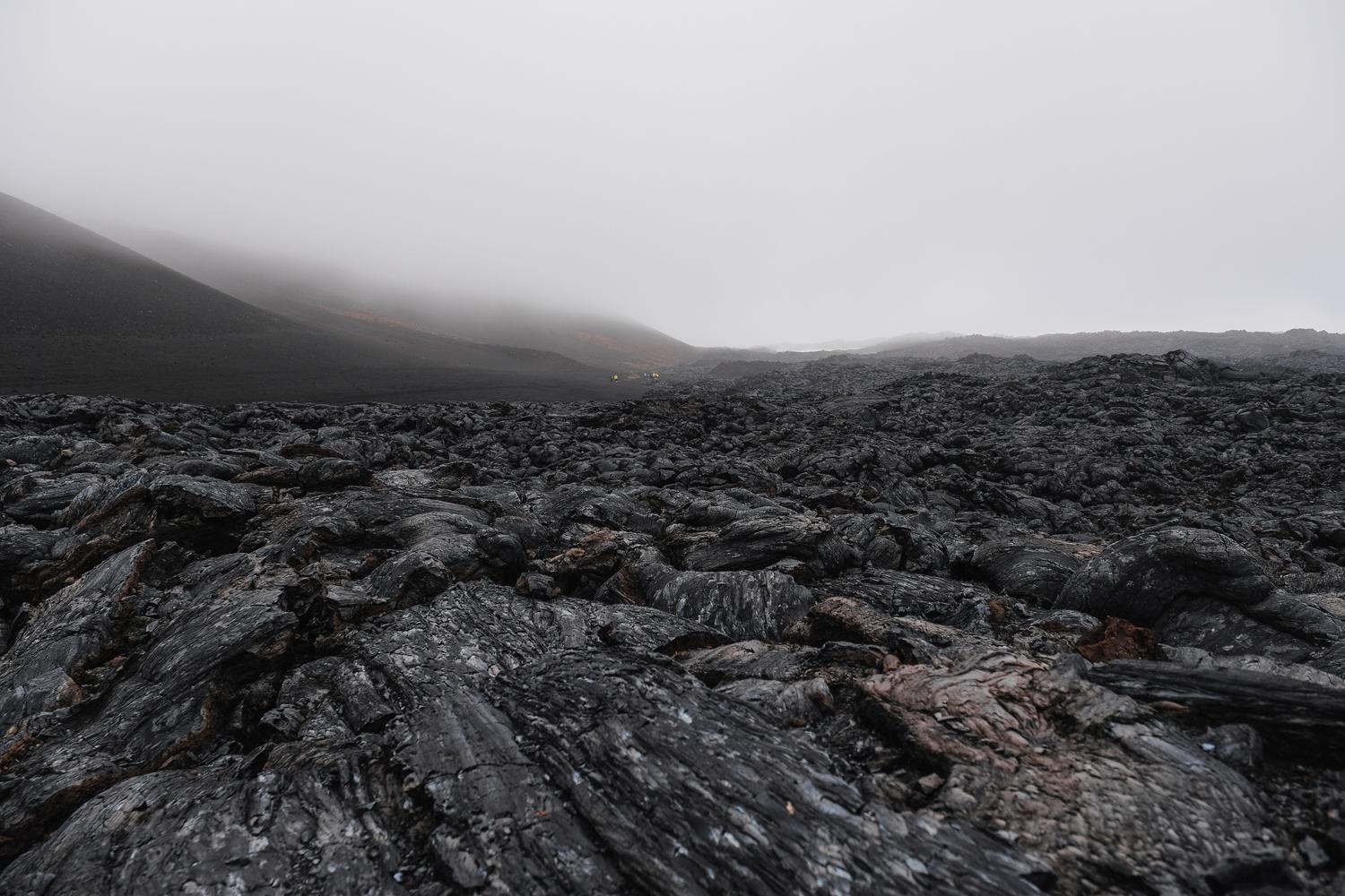 Paisaje volcánico oscuro con coladas de lava y niebla, creando un entorno hostil y misterioso Paisaje volcánico oscuro con coladas de lava y niebla, creando un entorno hostil y misterioso