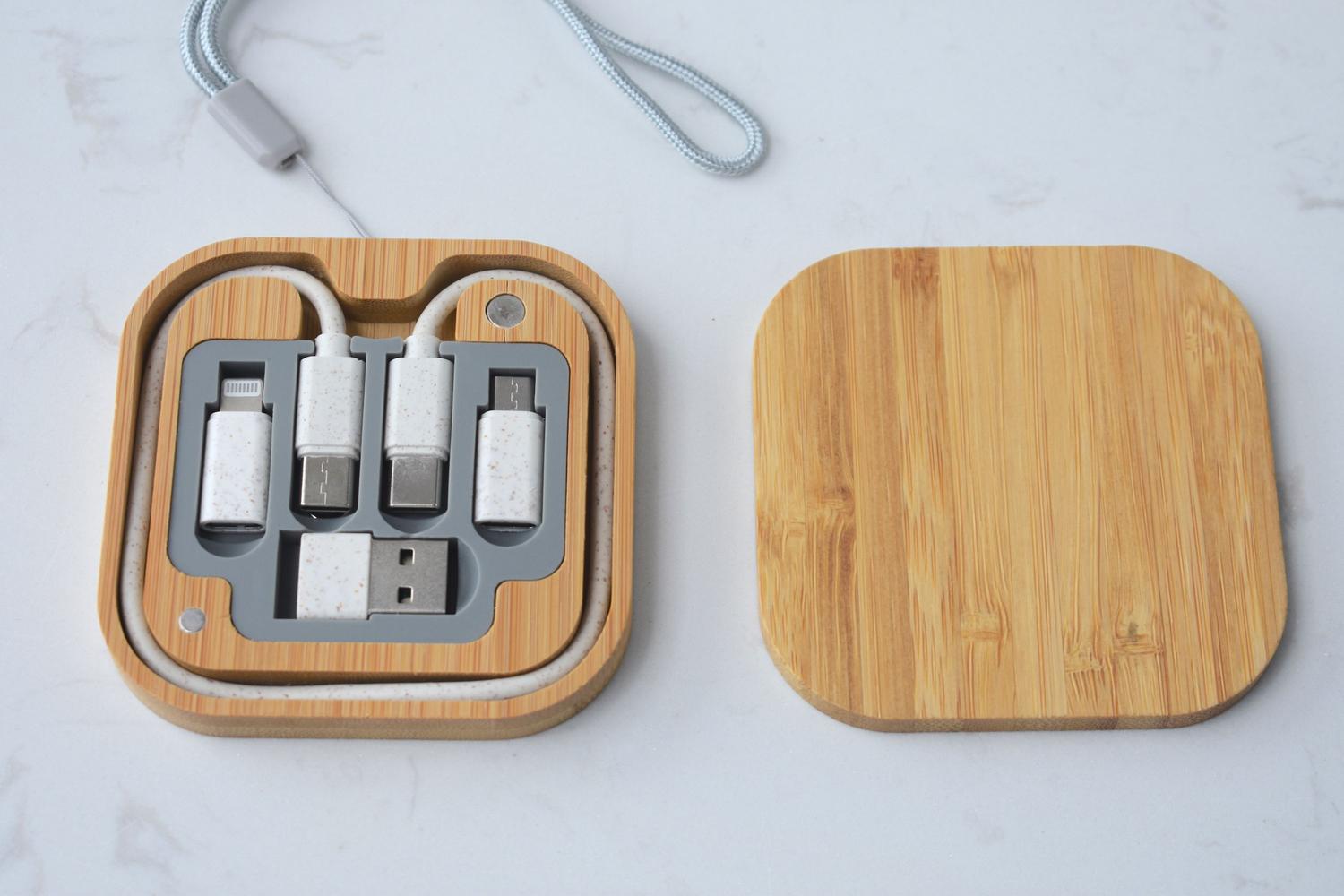 Caja organizadora de cables de bambú con conectores USB y adaptadores sobre una superficie blanca