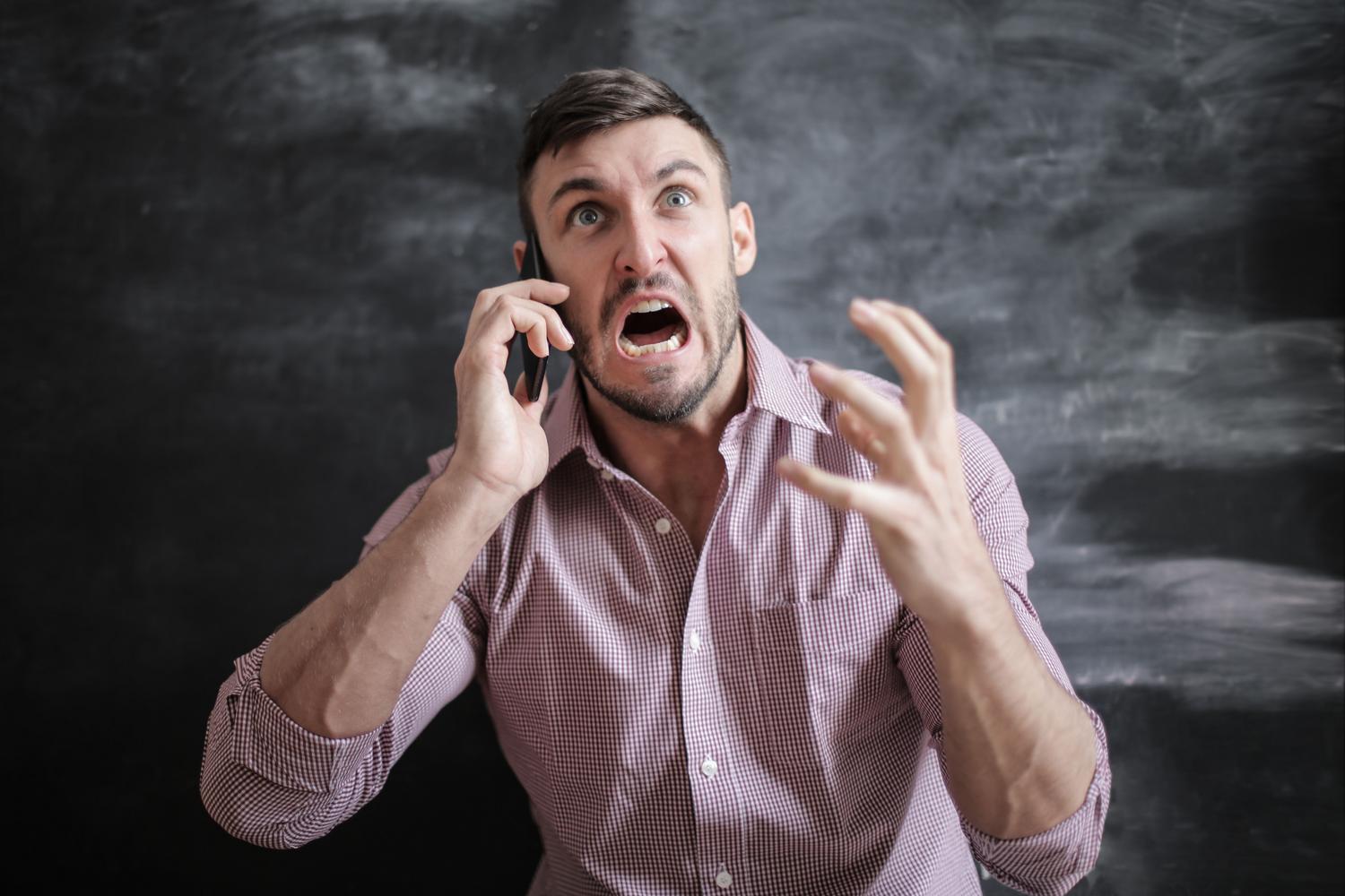 Hombre frustrado utilizando un teléfono inteligente en interiores, ilustrando la dificultad al resolver problemas técnicos.