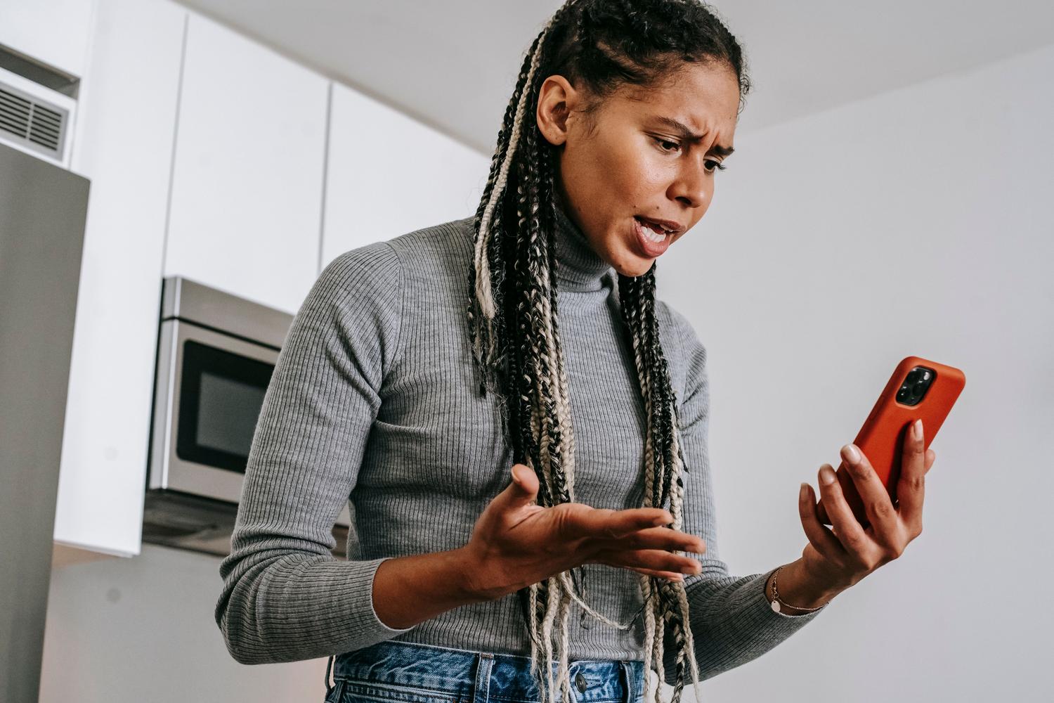 Mujer expresando molestia mientras usa su smartphone, representando la experiencia de usuario ante fallos tecnológicos.
