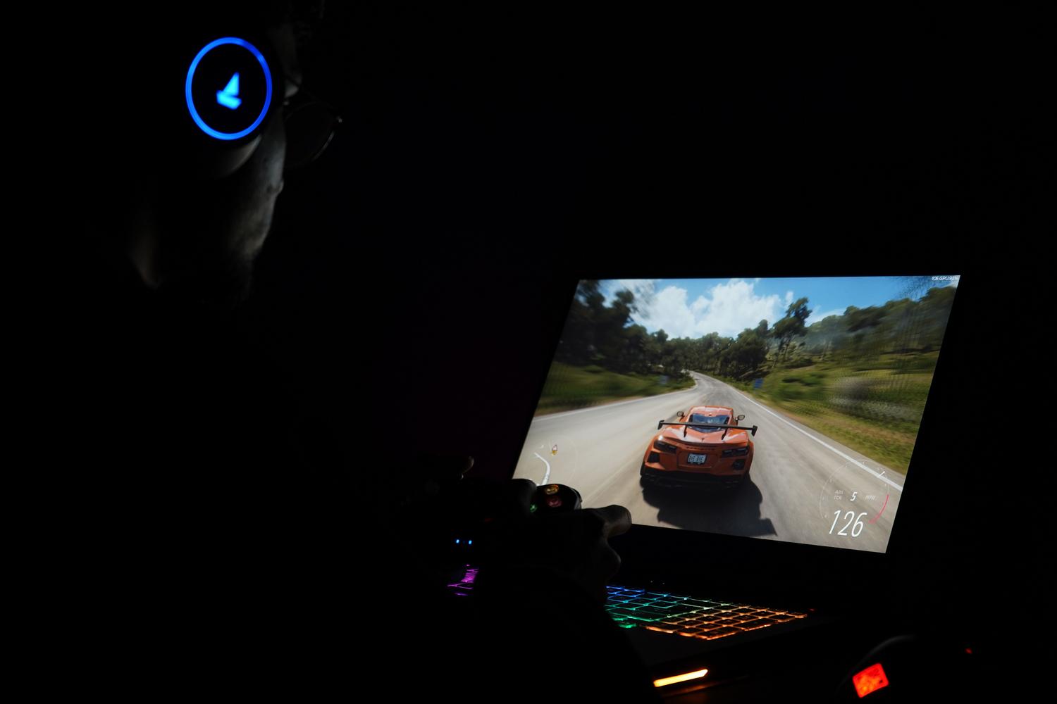 Jugador utilizando un portátil gaming y auriculares para jugar a un simulador de carreras en un entorno oscuro.