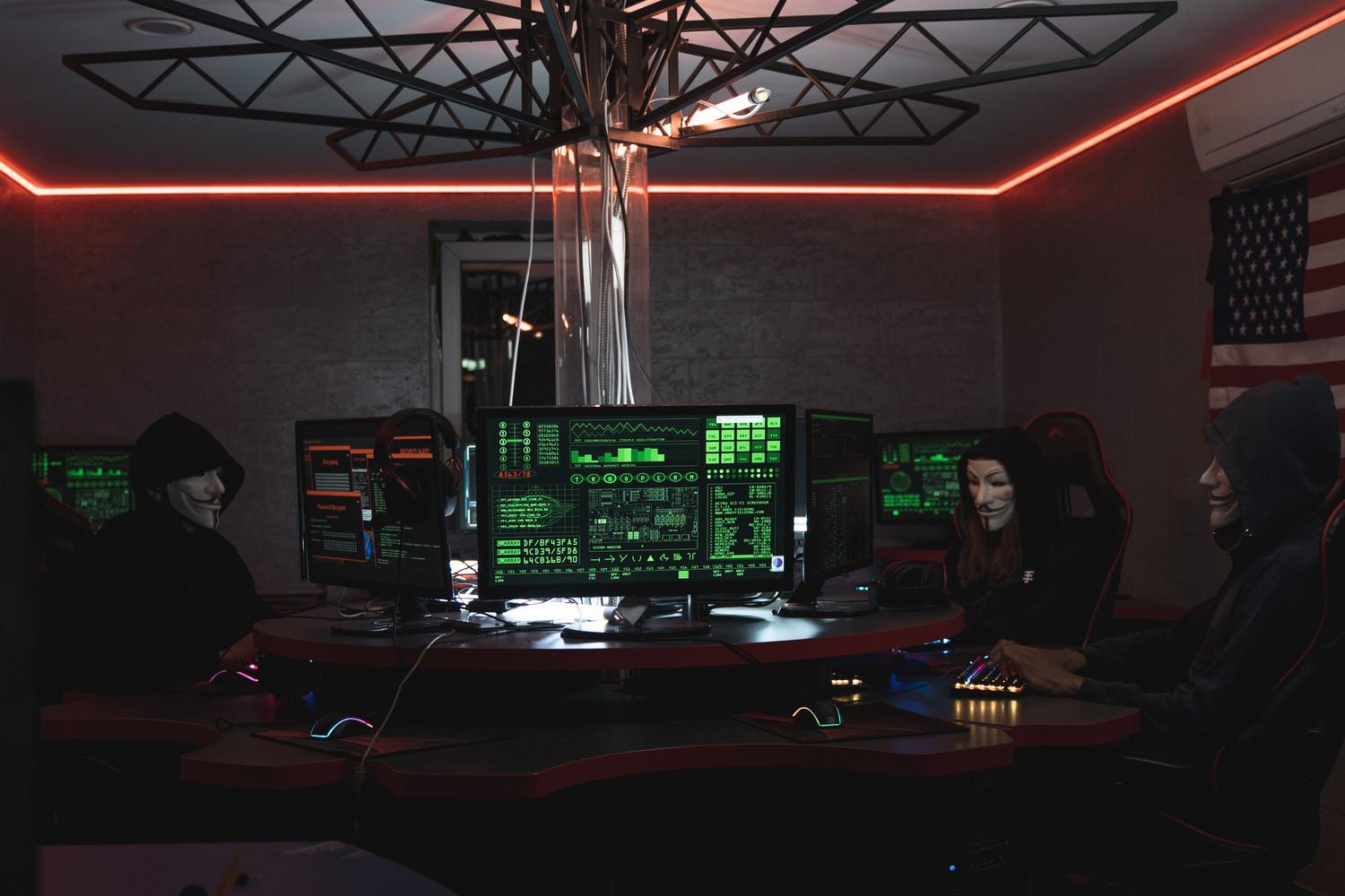 Grupo de hackers con máscaras de Guy Fawkes operando computadoras en un entorno oscuro, simbolizando las vulnerabilidades y ataques.