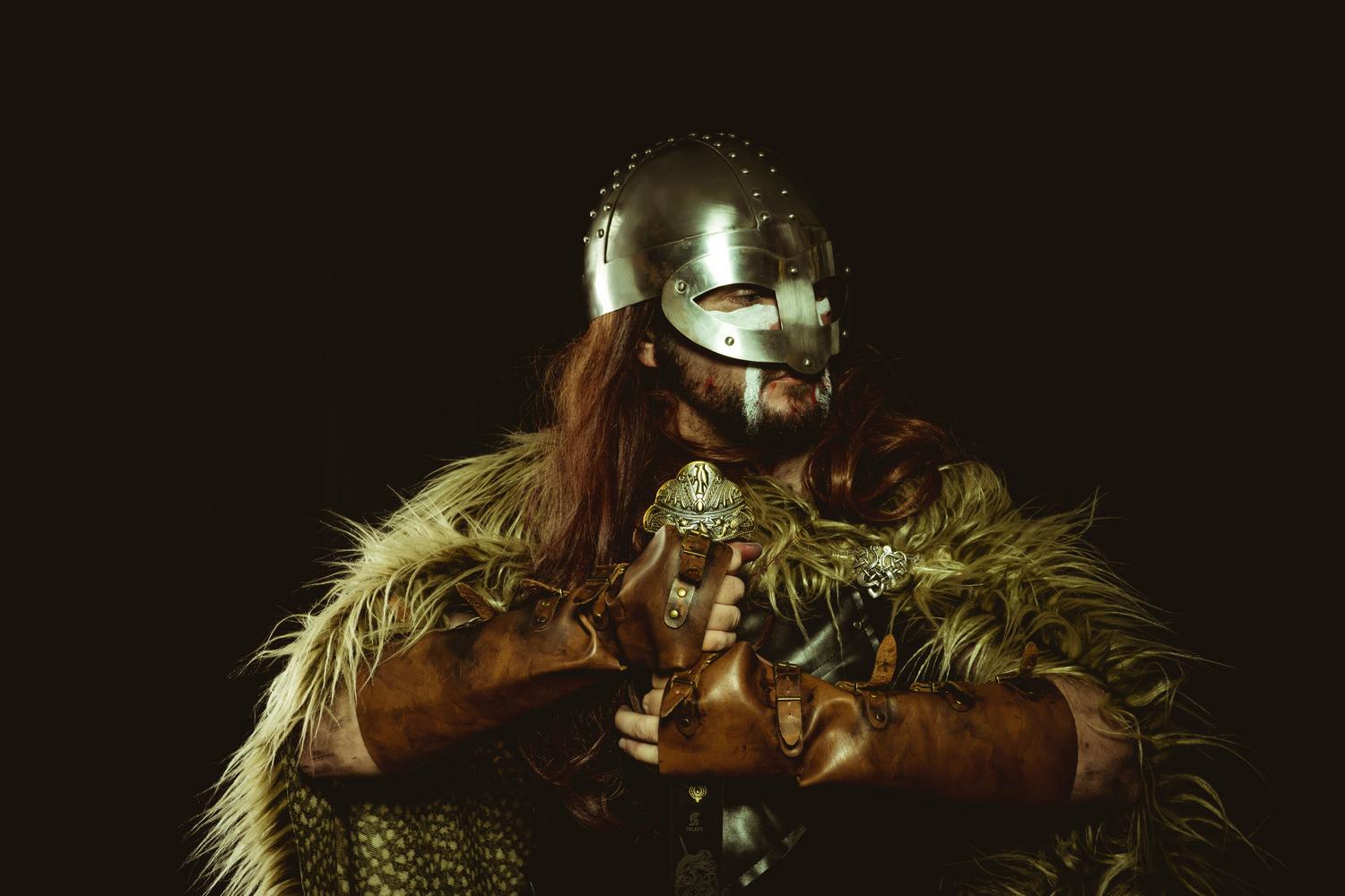 Guerrero vikingo con armadura, casco de metal y capa de piel sobre fondo oscuro, representando la épica del Viking Metal.