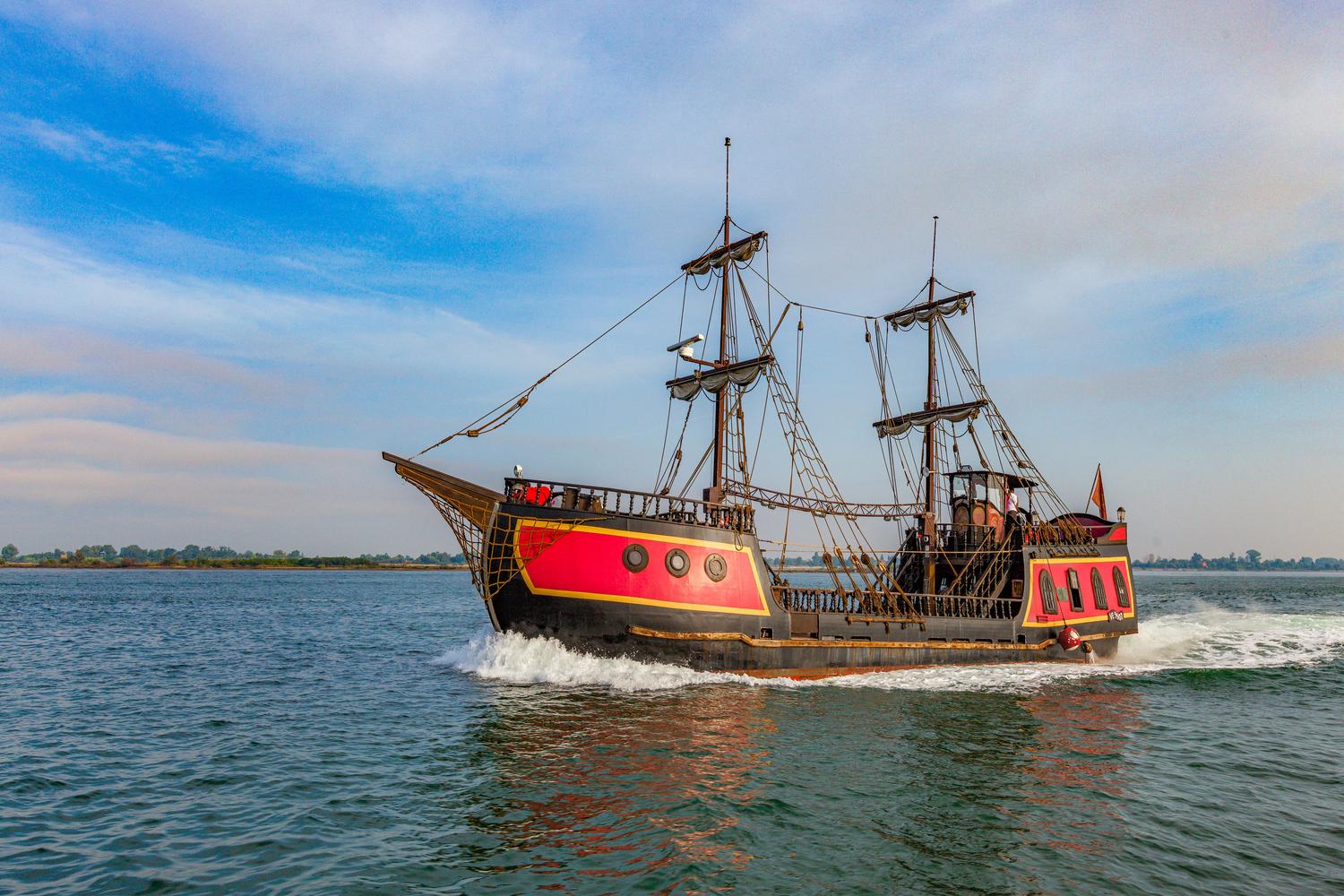 Majestuoso barco pirata con casco negro y rojo navegando en el océano azul, ilustrando la temática del Pirate Metal. Majestuoso barco pirata con casco negro y rojo navegando en el océano azul, ilustrando la temática del Pirate Metal.