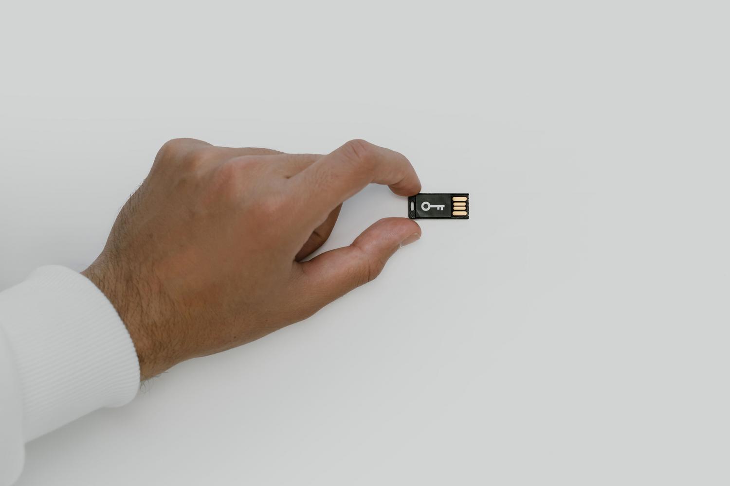 Mano sosteniendo una pequeña memoria USB con el símbolo de una llave, representando la seguridad digital y el cifrado de datos.
