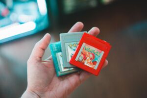 Mano sosteniendo cartuchos originales de Pokémon Red, Silver y Crystal, evocando la nostalgia de la primera y segunda generación.