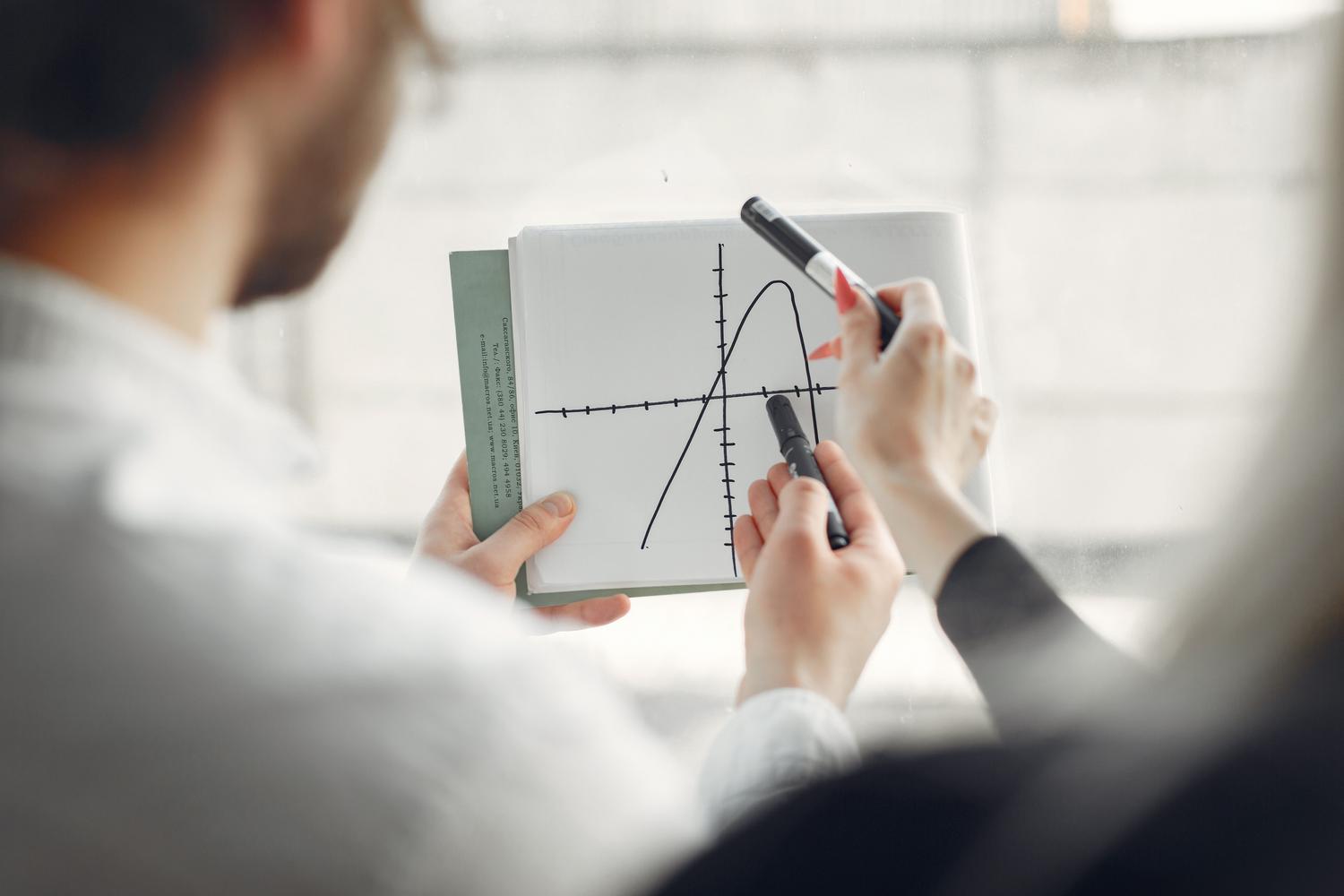 Dos profesionales colaborando y discutiendo la interpretación de un gráfico de datos en un cuaderno.