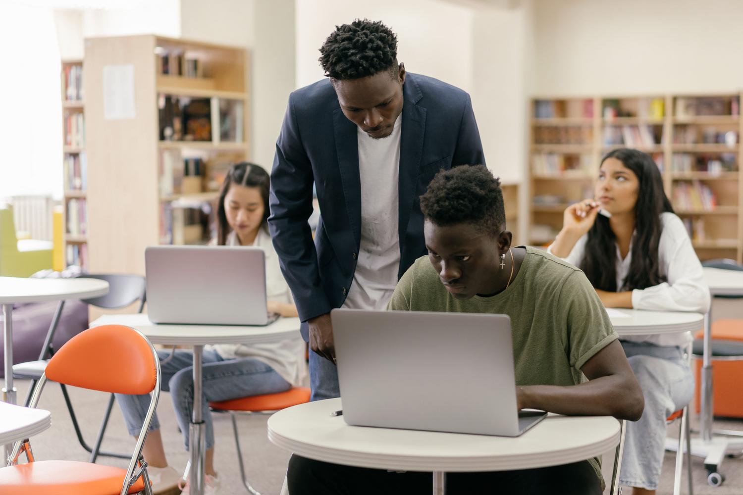 Estudiantes utilizando ordenadores portátiles en un aula moderna con la supervisión de un profesor, ilustrando el uso estándar de los Chromebooks en el sector educativo.