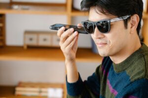 Hombre con discapacidad visual utilizando la cámara de su smartphone en posición horizontal para escanear el entorno, representando el uso de un asistente de visión por IA como Guided Vision de Google.