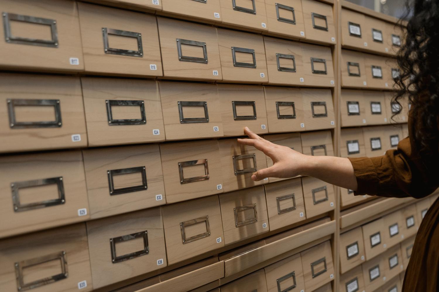 Persona organizando cajones de madera en una sala de archivos, representando la gestión tradicional de fuentes históricas.