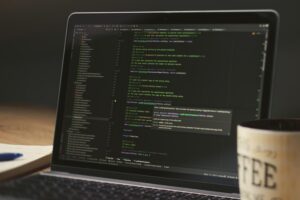 Espacio de trabajo de un programador con un portátil mostrando código y una taza de café, representando el flujo de trabajo de desarrollo.