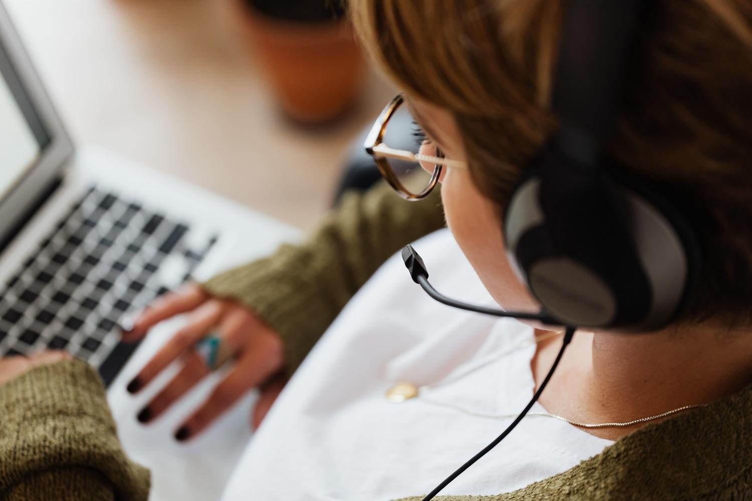Mujer utilizando auriculares con micrófono incorporado mientras trabaja en su ordenador portátil desde una perspectiva cenital.