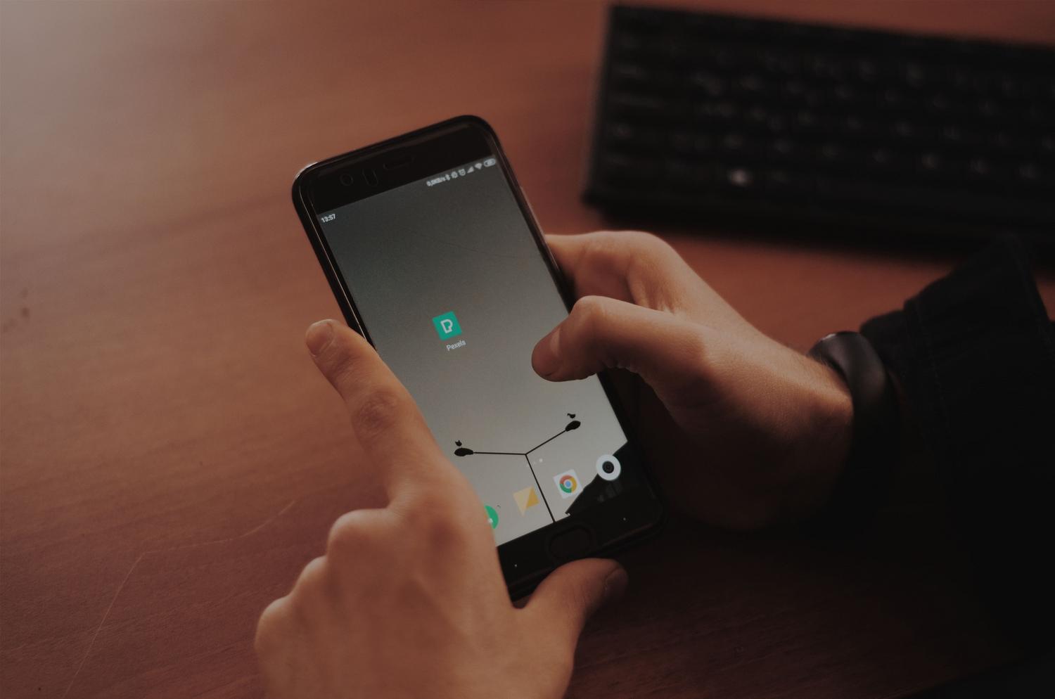 Primer plano de manos interactuando con la pantalla de un smartphone sobre un escritorio de madera.