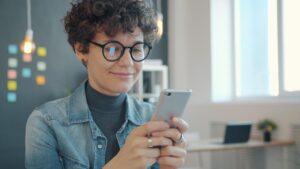 Mujer profesional utilizando un smartphone en una oficina moderna y luminosa, representando la productividad.