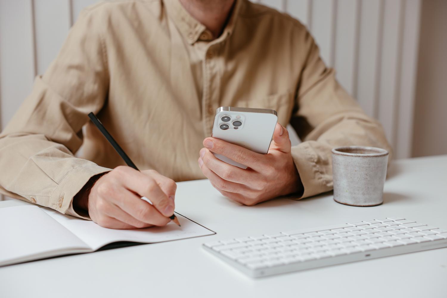 Persona organizando su día con un smartphone y un cuaderno en un escritorio, ilustrando la eficiencia y planificación.
