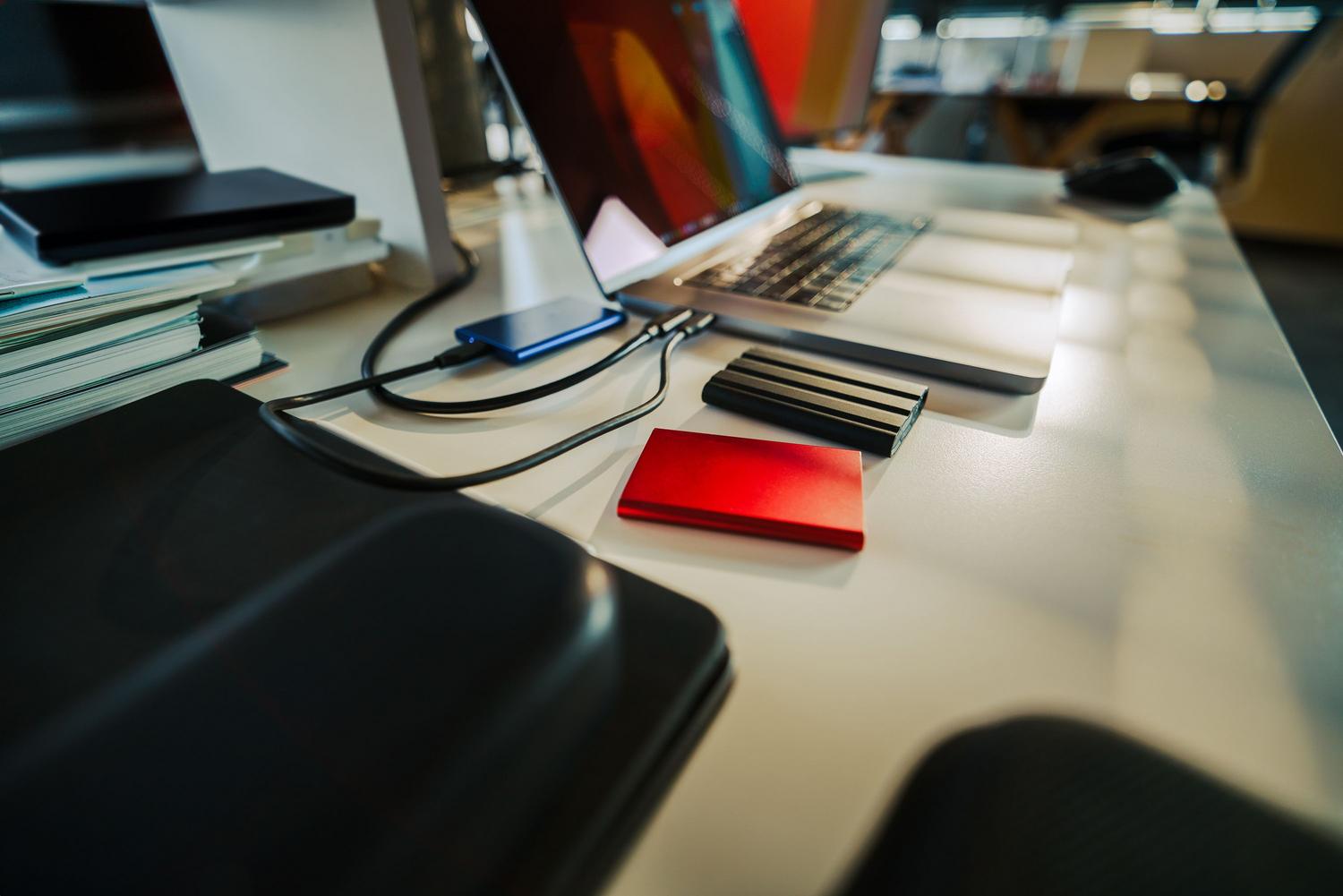 Escritorio de oficina organizado con un portátil y varios discos duros externos para copias de seguridad