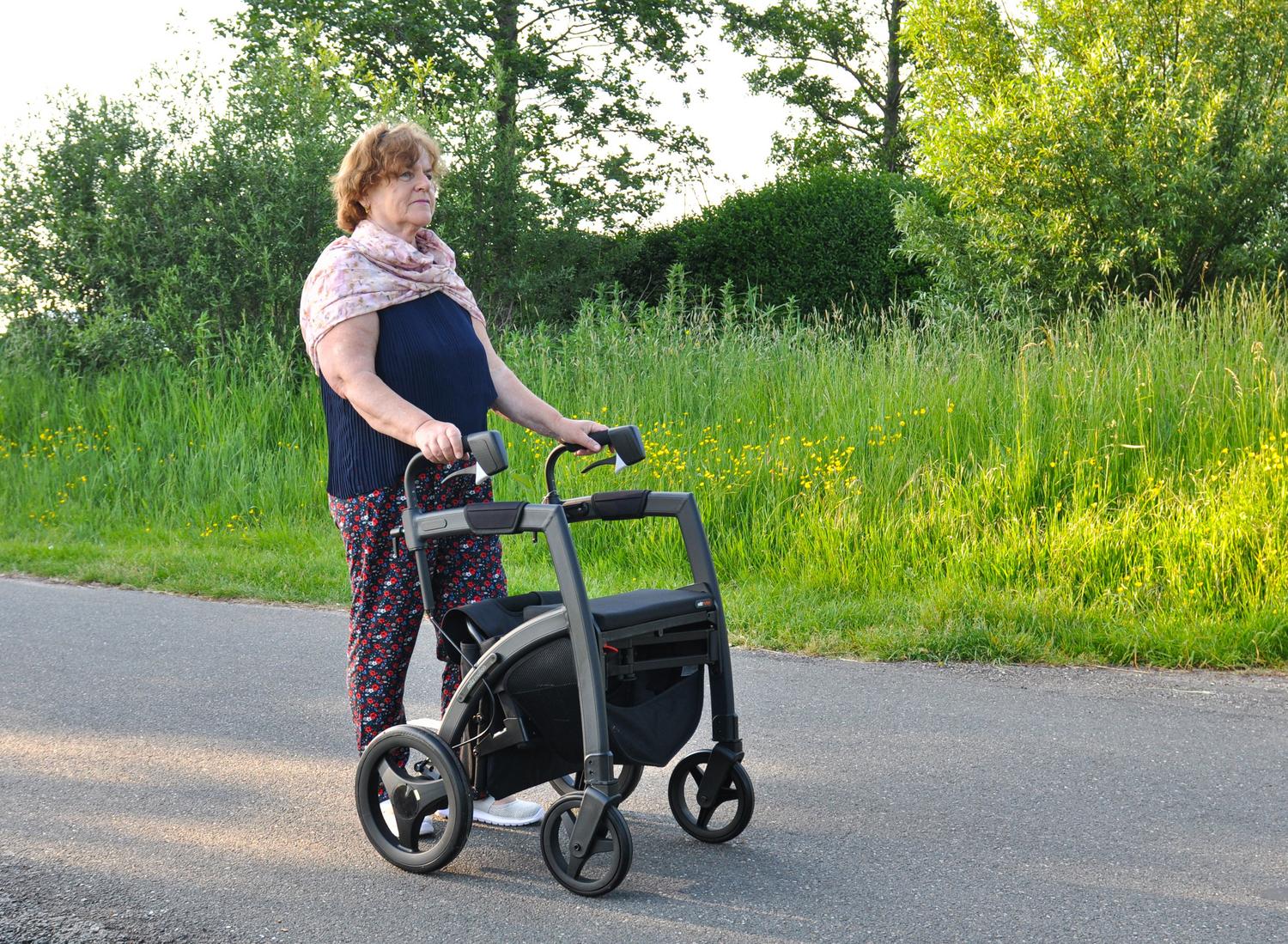 Mujer mayor utilizando un andador rollator en un parque, ilustrando las ayudas técnicas para mantener la movilidad y autonomía.
