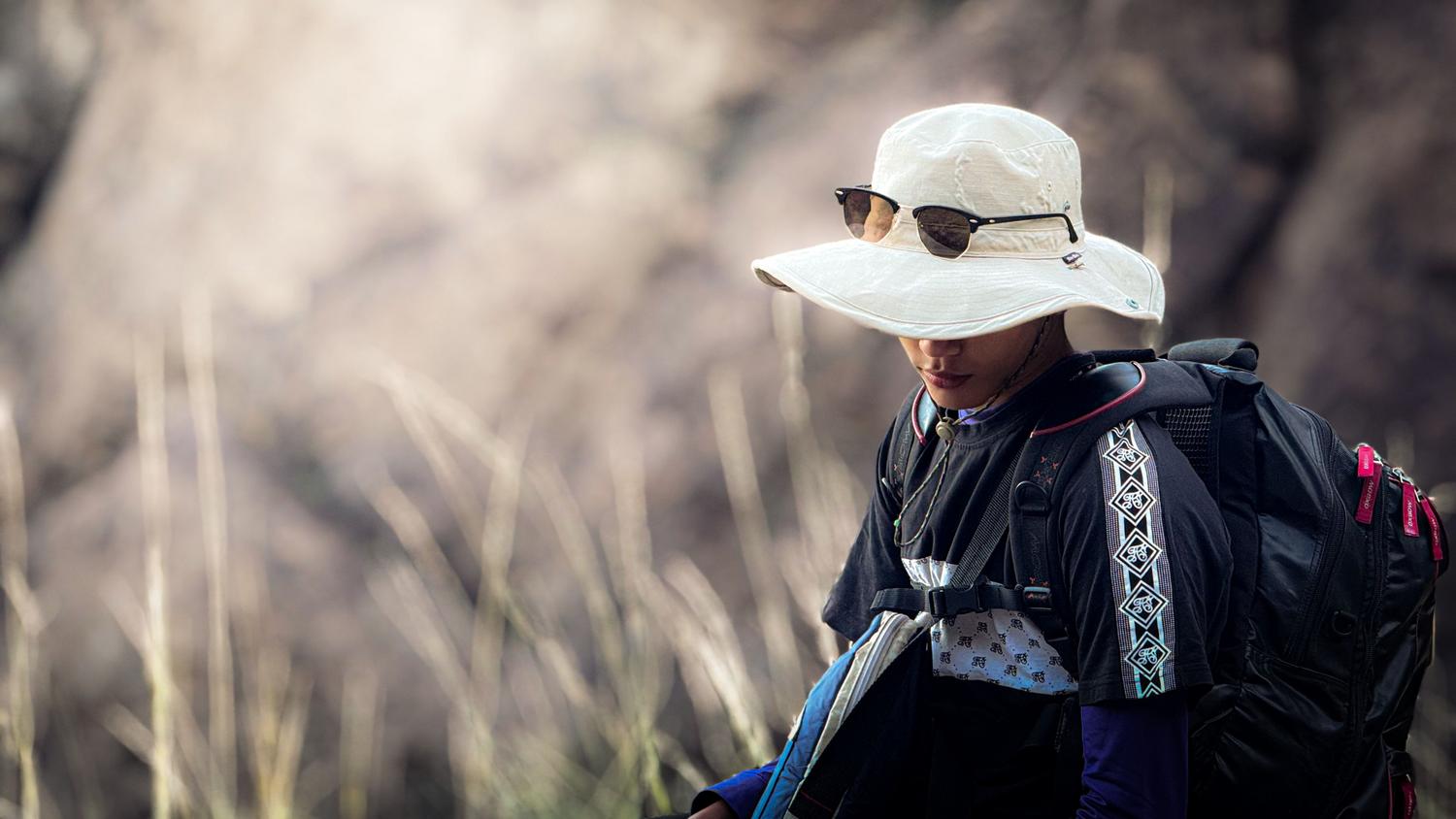 Hombre con sombrero y gafas de sol practicando senderismo en verano, utilizando ropa ligera para protegerse de los rayos UV