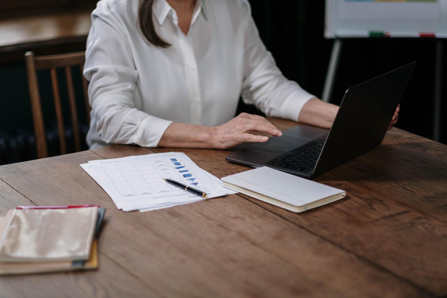 Mujer de negocios analizando hojas de cálculo y gráficos en su escritorio, enfocada en la organización de datos.