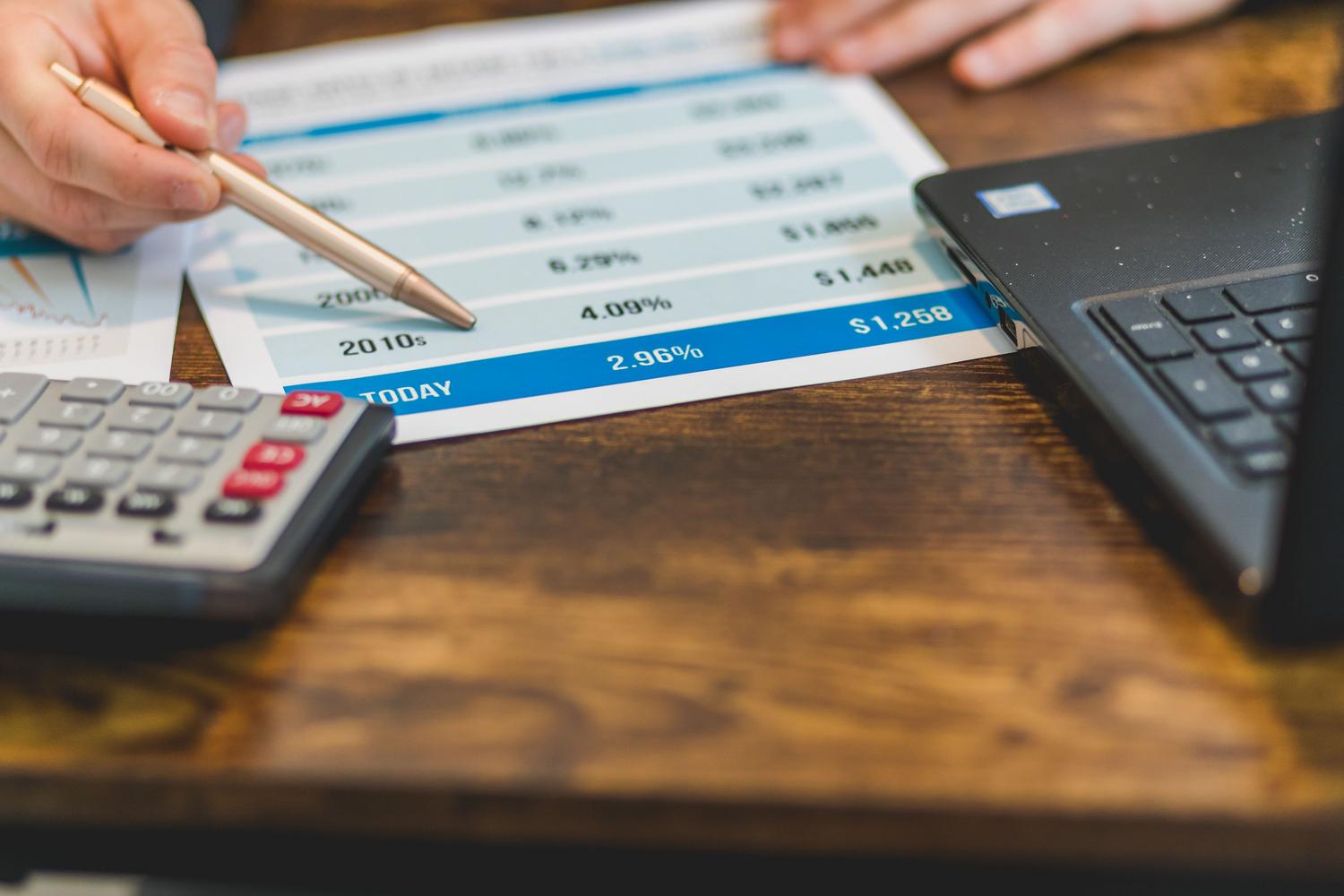 Primer plano de tablas de datos impresas junto a un portátil, representando la revisión y conversión de magnitudes numéricas.
