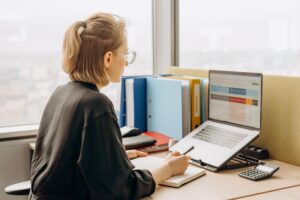 Mujer profesional trabajando en una hoja de cálculo de Excel con una calculadora al lado, ideal para ilustrar el análisis de datos y conversiones.