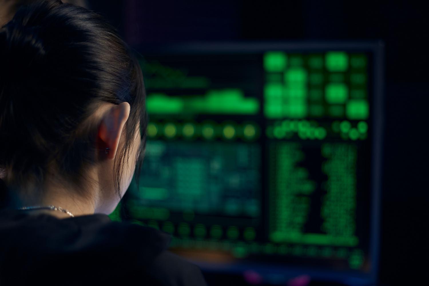 Analista de seguridad concentrado examinando datos técnicos en un monitor en un entorno de baja iluminación.