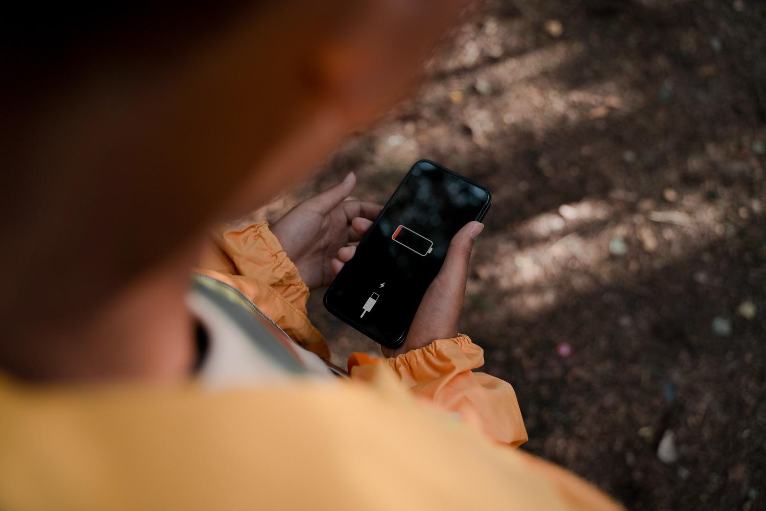 Joven sosteniendo un smartphone que muestra el aviso de batería baja en un bosque, relacionándolo con la pérdida de conexión por falta de energía.