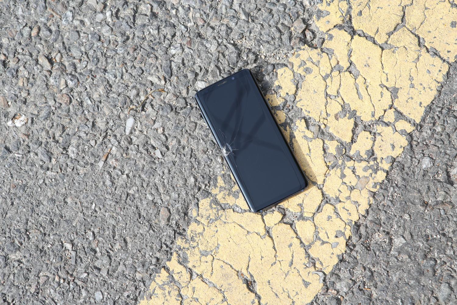Primer plano de un smartphone con la pantalla rota sobre el asfalto, ilustrando un dispositivo perdido y dañado.