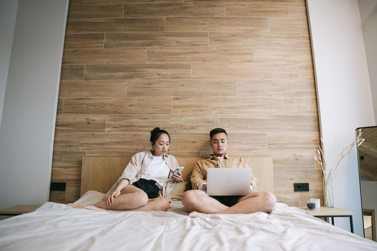 Pareja utilizando dispositivos electrónicos en un dormitorio, ilustrando la necesidad de cobertura WiFi en todas las estancias de la casa.