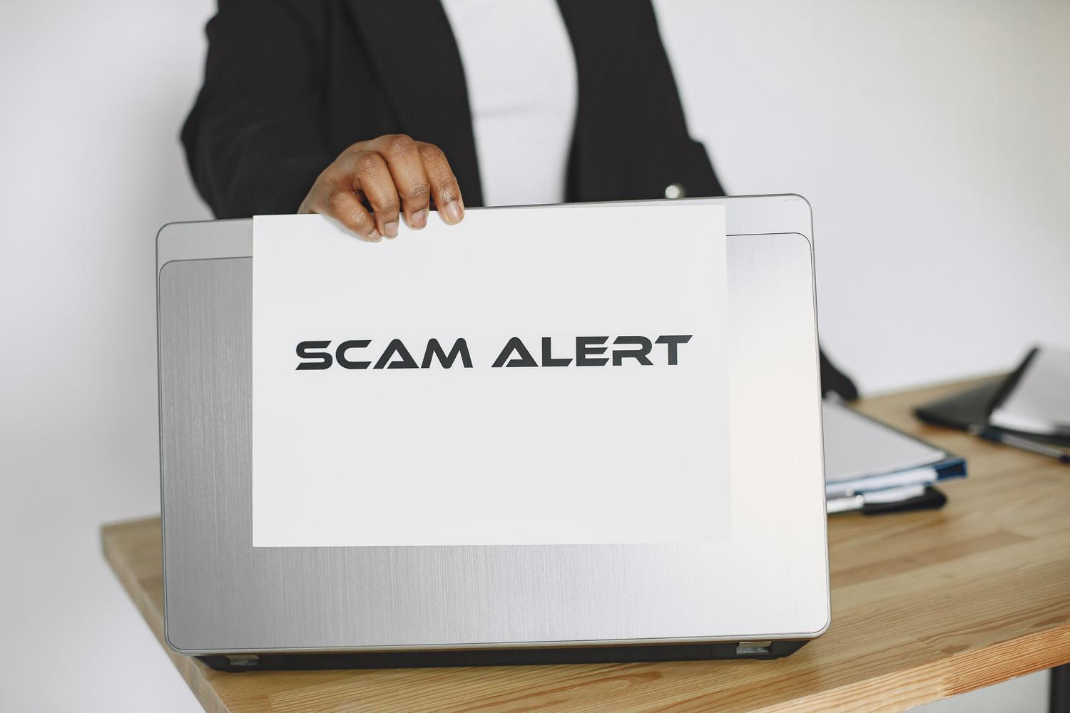 Cartel de 'SCAM ALERT' sobre un ordenador portátil, simbolizando el peligro de los engaños digitales.