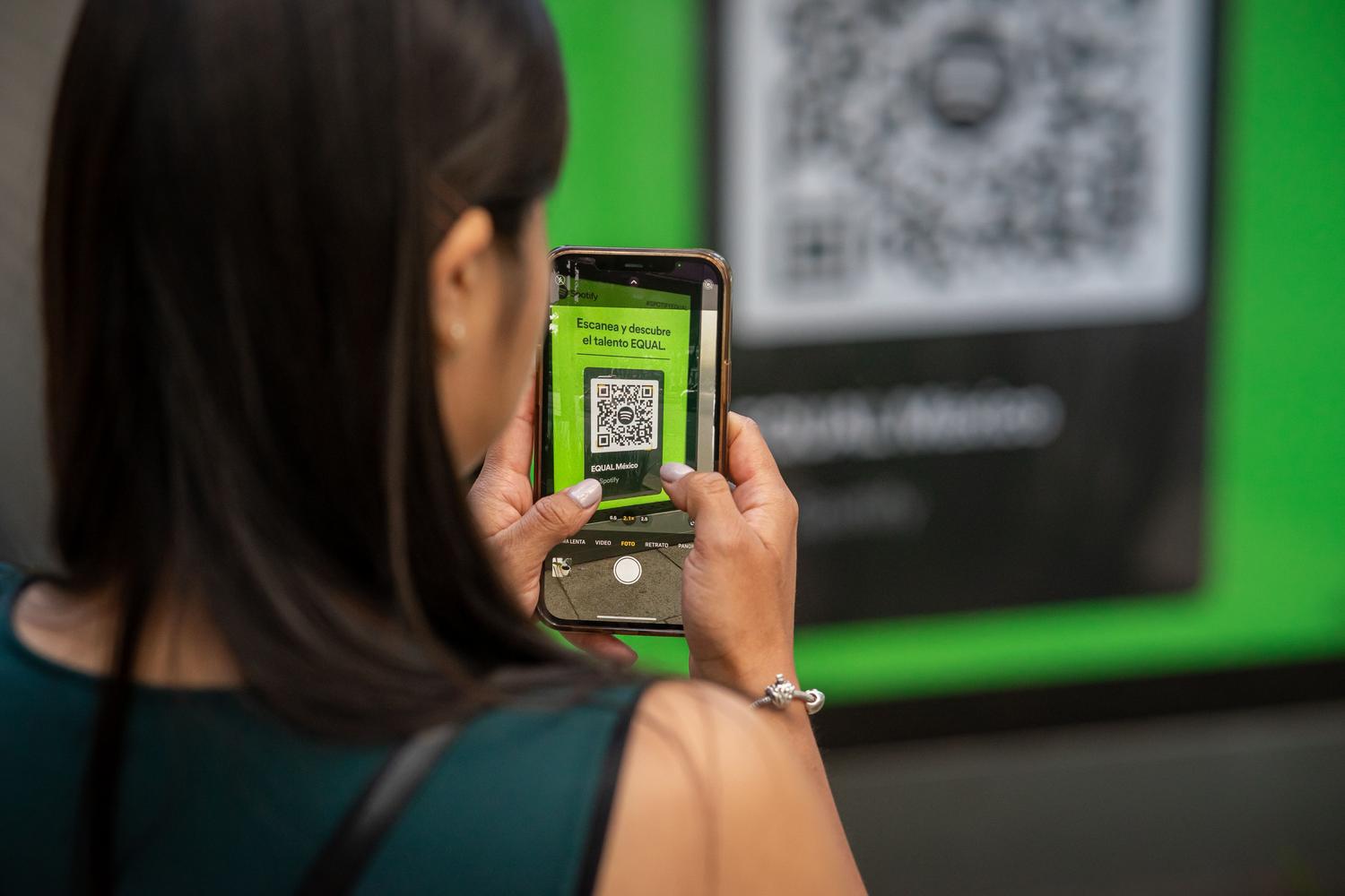Mujer escaneando un código QR con su teléfono móvil en la calle, representando la facilidad de uso para el consumidor final.