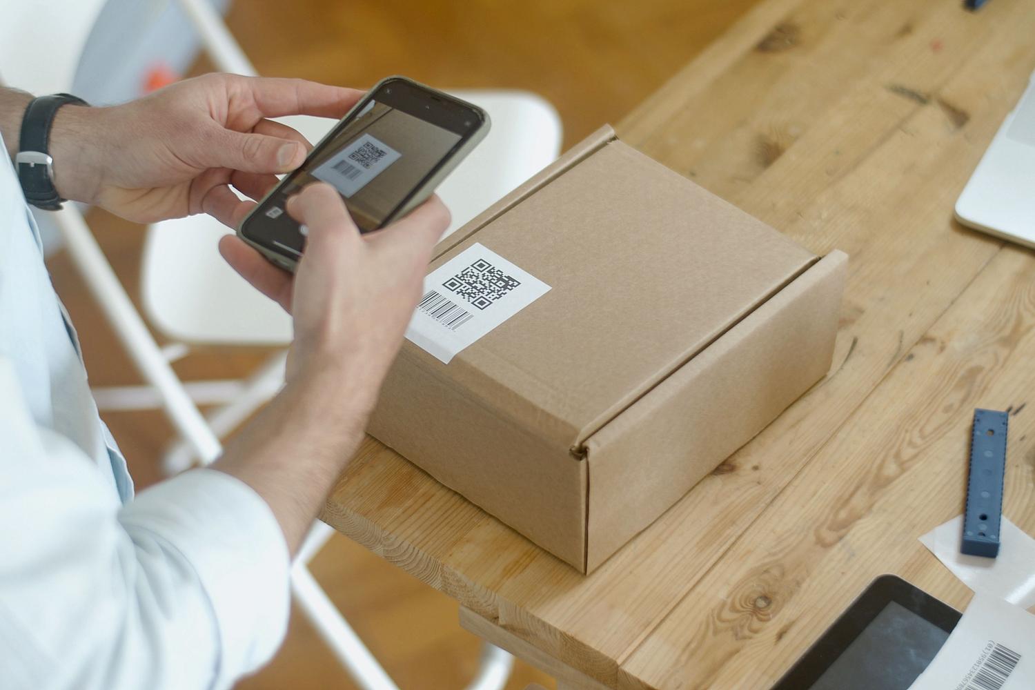 Persona escaneando un código QR en el embalaje de un producto, ejemplificando la aplicación de QRs en logística y gestión de productos.