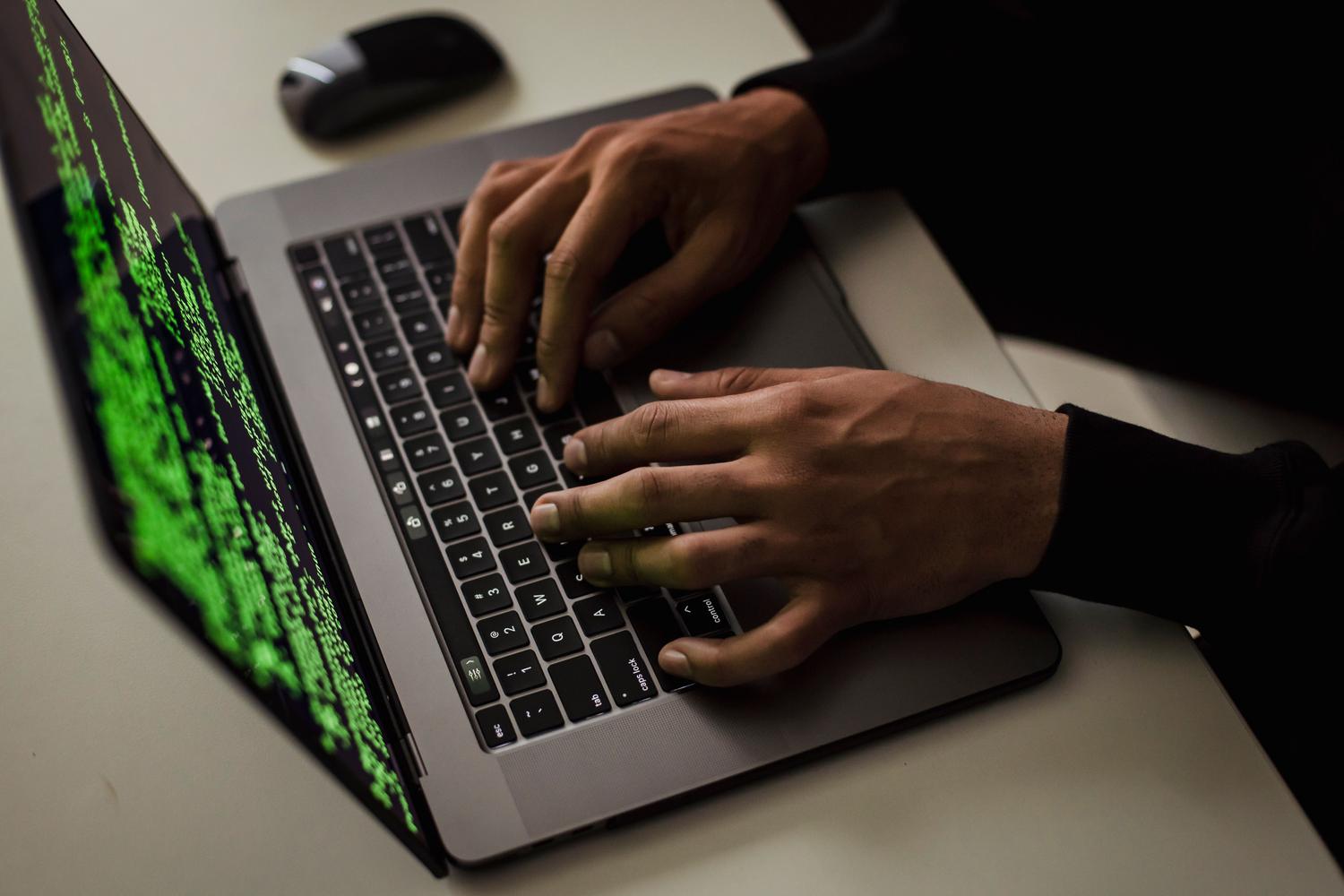 Manos de un hacker escribiendo código en un ordenador en un entorno oscuro, ilustrando las amenazas digitales.