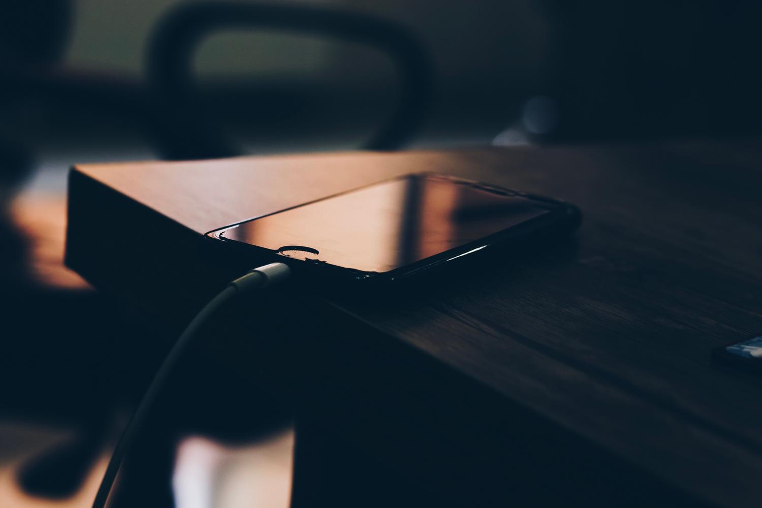 Teléfono móvil conectado a su cargador sobre una mesa de madera.