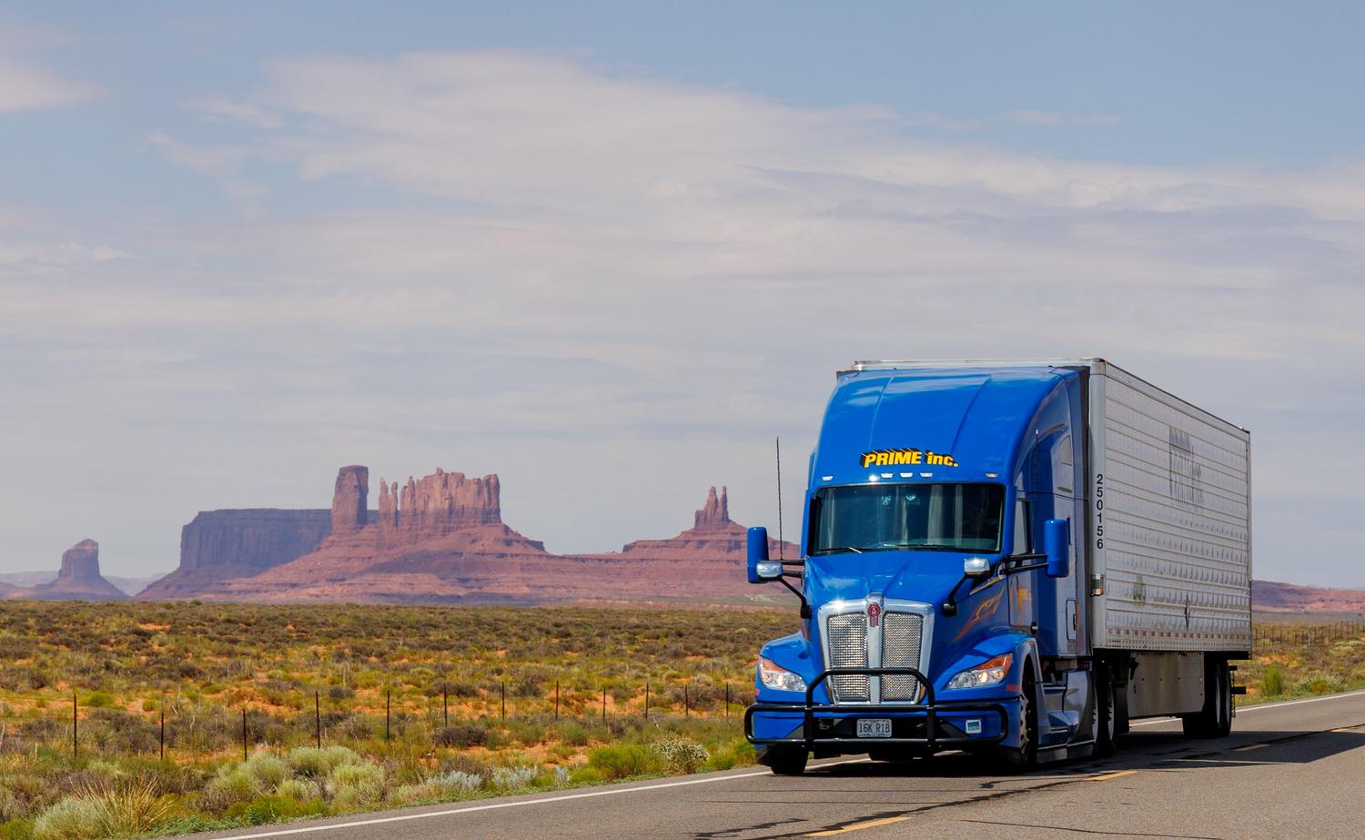 Camión azul circulando por una carretera con los icónicos paisajes de Monument Valley al fondo, destacando la inmensidad de Norteamérica. Camión azul circulando por una carretera con los icónicos paisajes de Monument Valley al fondo, destacando la inmensidad de Norteamérica.