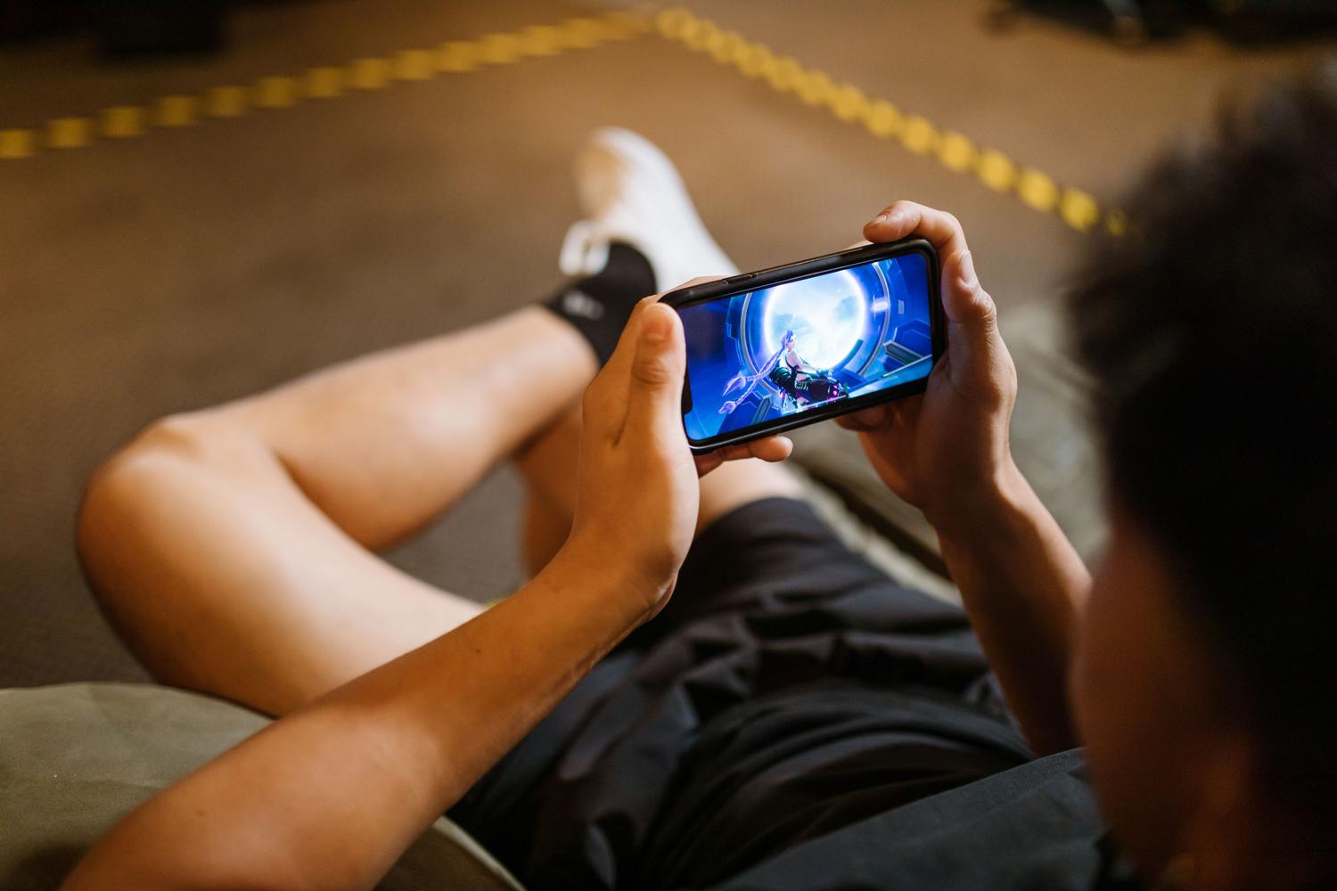 Persona jugando un videojuego en un smartphone, ilustrando la disponibilidad de Genshin Impact en dispositivos móviles.