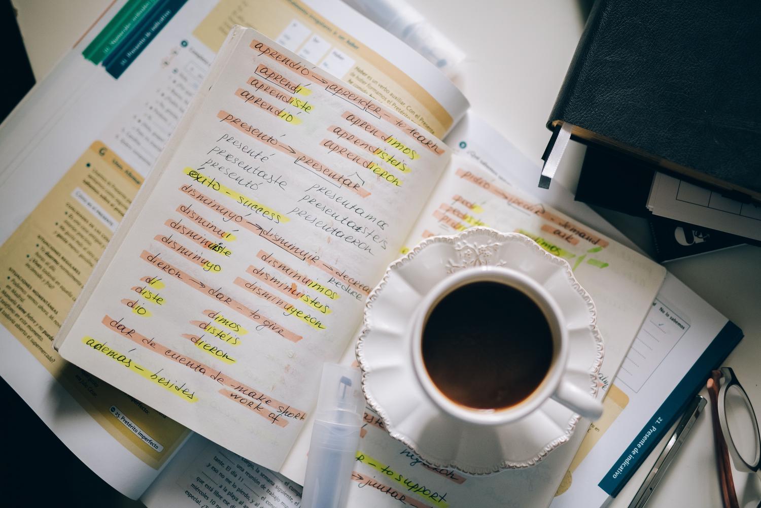 Apuntes manuscritos sobre el aprendizaje del español acompañados de una taza de café.