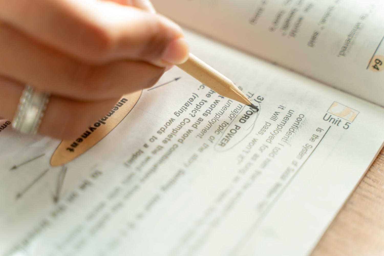 Mujer estudiando vocabulario y gramática en un libro de texto con un lápiz.