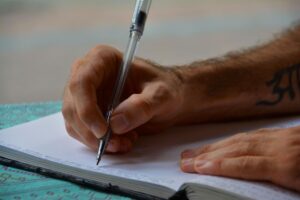 Primer plano de una persona escribiendo en un cuaderno, ideal para ilustrar el estudio de la gramática y la ortografía.