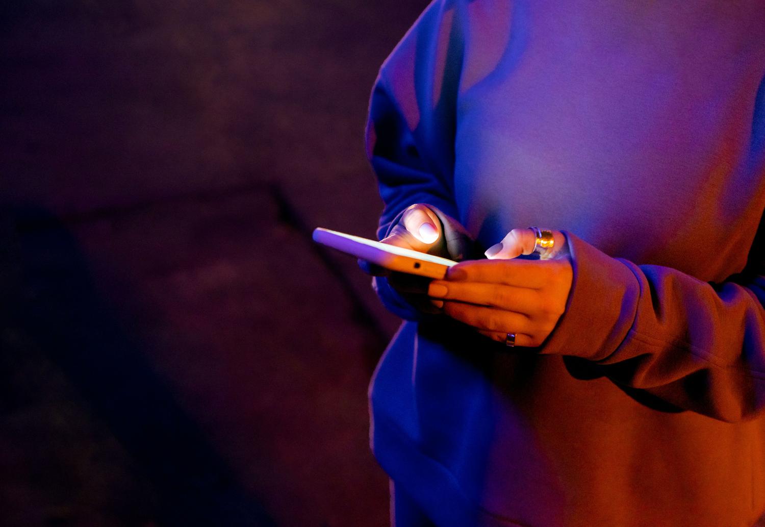 Persona utilizando un smartphone en un ambiente nocturno con luces de neón, representando la importancia de la identificación en fiestas o eventos.