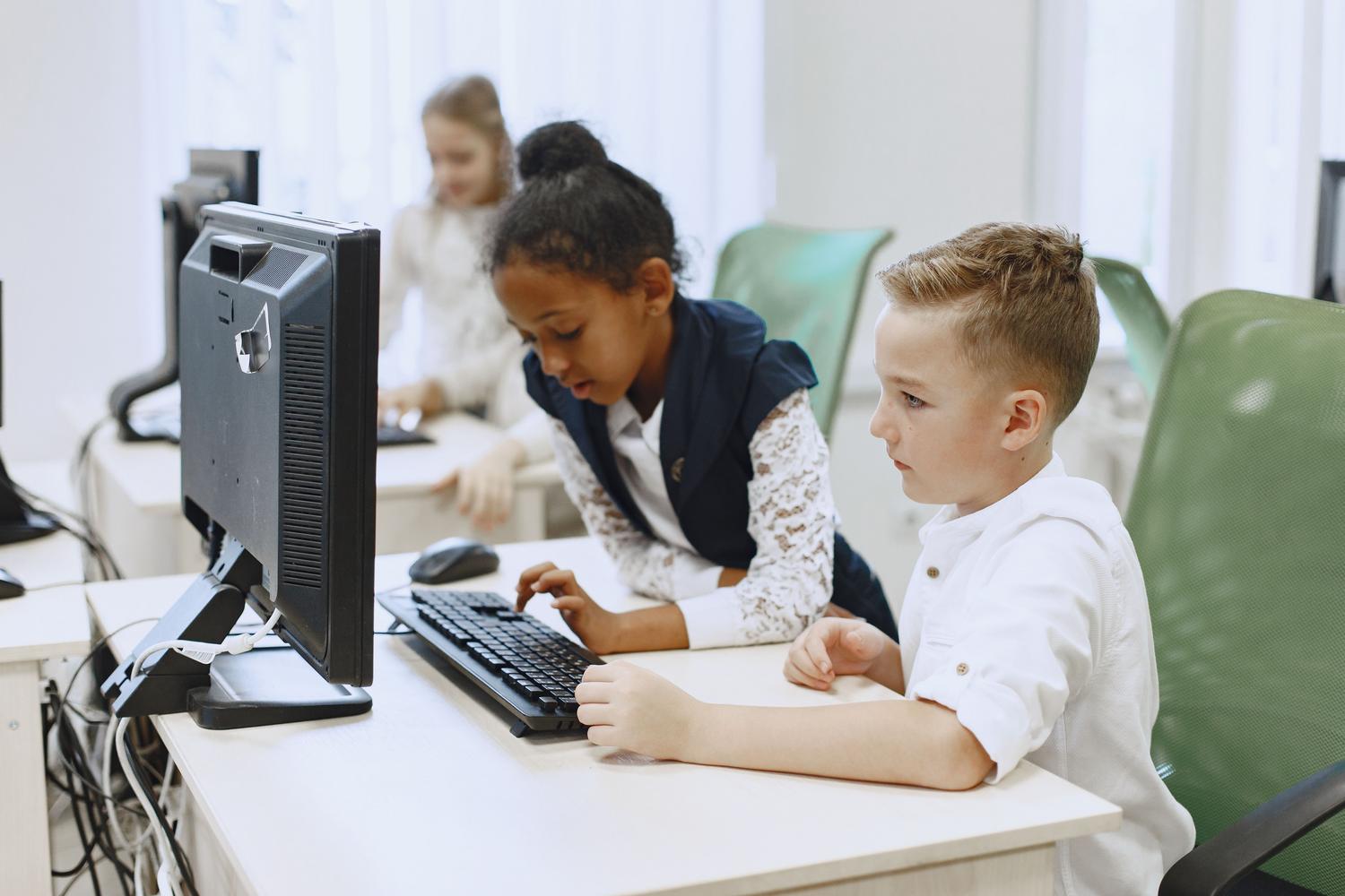 Grupo diverso de niños utilizando ordenadores en un aula moderna, integrando la tecnología en la educación básica.