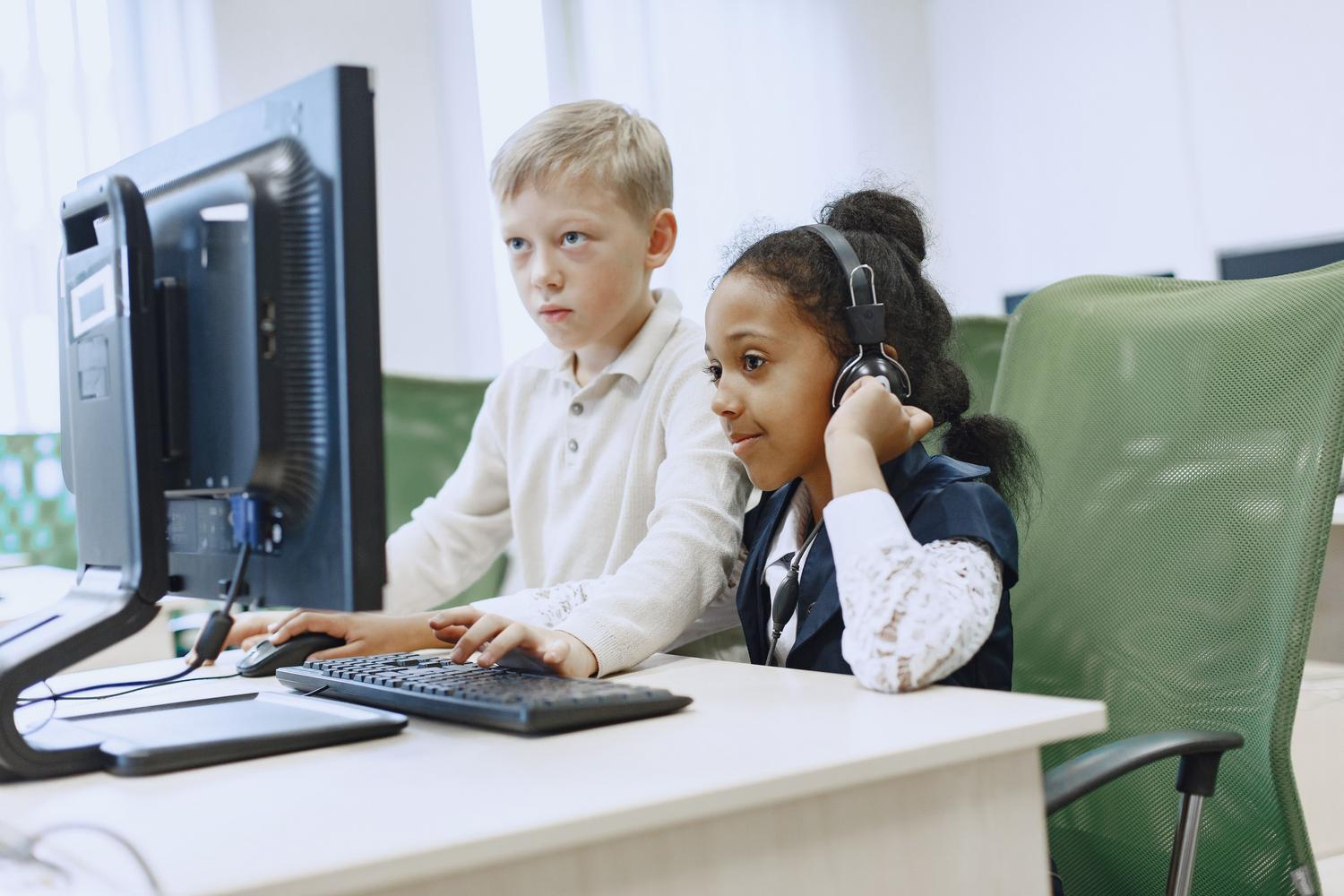 Dos niños trabajando juntos en un laboratorio de informática, fomentando el aprendizaje colaborativo en el aula de primaria.